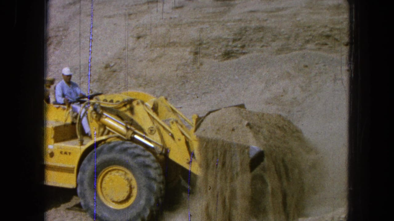 The 1965 Pueblo, Mexico home-movie frame shows a worker lifting sand in a yellow Caterpillar front-end loader.