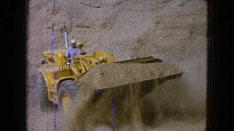 A front-facing view shows the yellow loader moving sand through dust at the Pueblo, Mexico work site in 1965 footage.