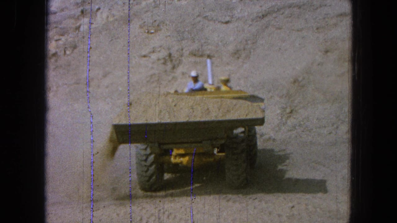 Rear view of the yellow quarry loader in Pueblo, Mexico, with large tires, dust, and a hard-hatted operator visible in 8mm footage.