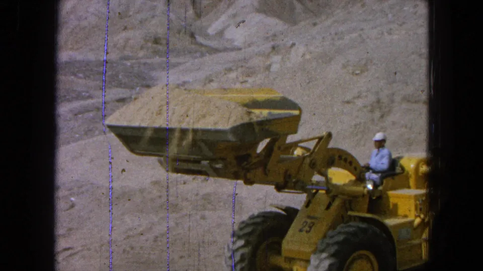 Side view of a yellow front-end loader and hard-hatted operator working in a quarry, supported by the supplied 1965 Pueblo, Mexico metadata.