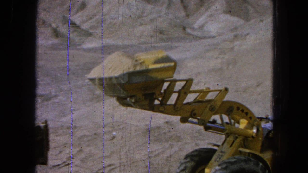 Yellow front-end loader carries dirt in its raised bucket beside an excavated earth bank.