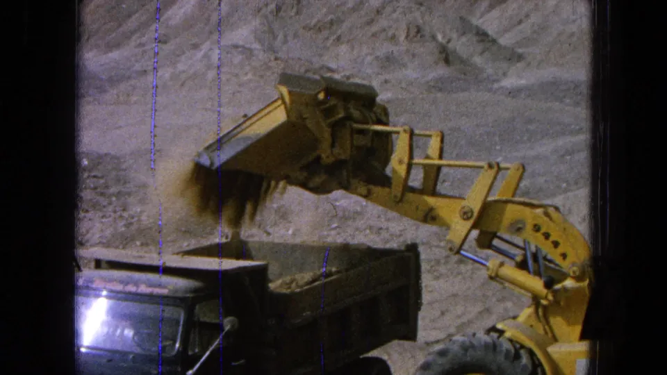 The loader tips its bucket and releases dirt into the dump truck bed at the 1965 Pueblo, Mexico construction site.