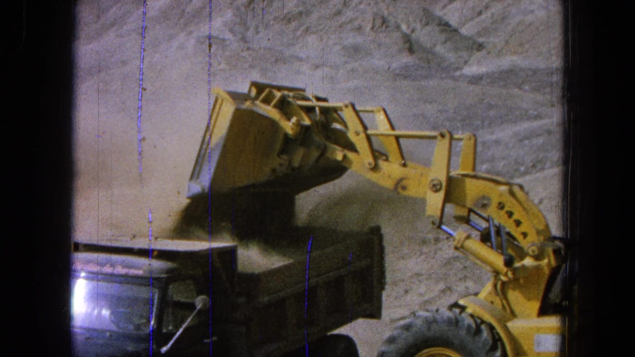 Yellow front-end loader appears to dump dirt into a dark truck bed at a Pueblo, Mexico construction site in 1965 home-movie footage.