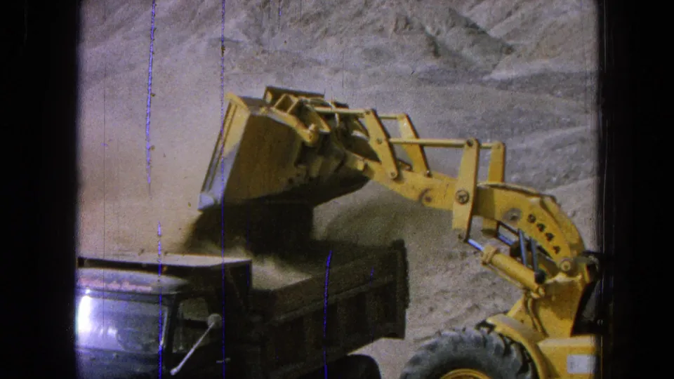 Yellow front-end loader appears to dump dirt into a dark truck bed at a Pueblo, Mexico construction site in 1965 home-movie footage.