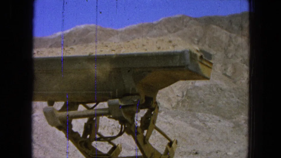 1965 Pueblo, Mexico 8mm frame focused on the dump truck bed and undercarriage in a dry quarry setting.