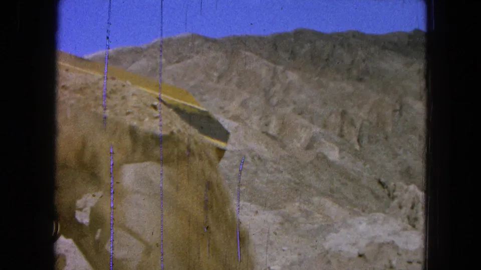 A dusty 1965 Pueblo, Mexico quarry frame shows earth spilling near a truck bed or loader bucket against rugged hills.