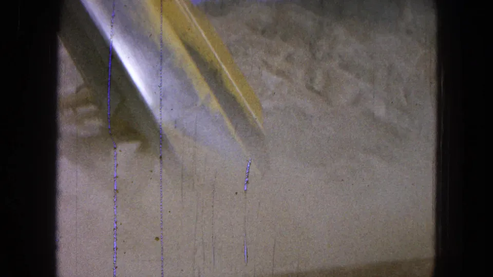 1965 Pueblo, Mexico 8mm frame showing the loader bucket angled down as dust and dirt spread below.