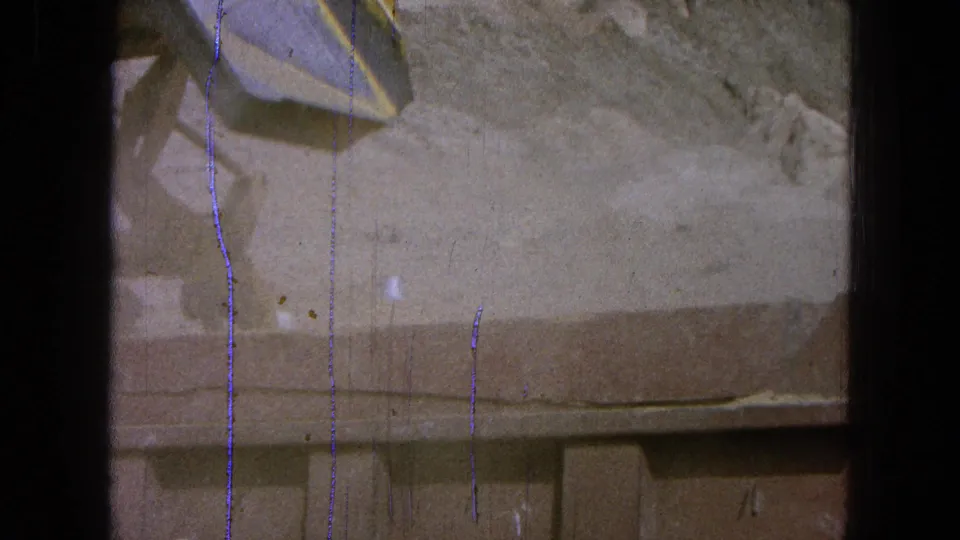 1965 Pueblo, Mexico 8mm frame with the loader bucket lowered beside dusty ground and rocky terrain.