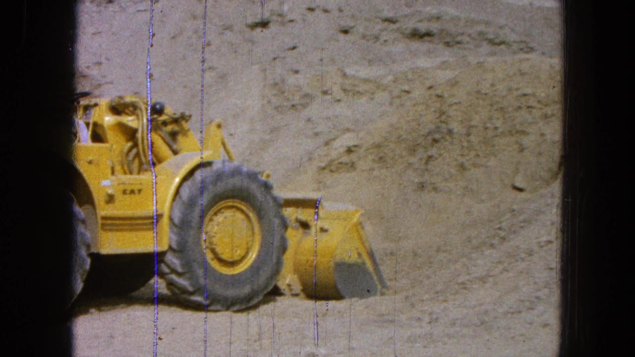 Yellow Caterpillar loader beside a dirt bank in a dusty quarry setting.