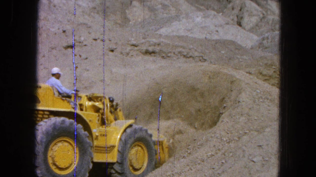 Yellow loader partly visible beside a sand pile with an operator in a white cap.