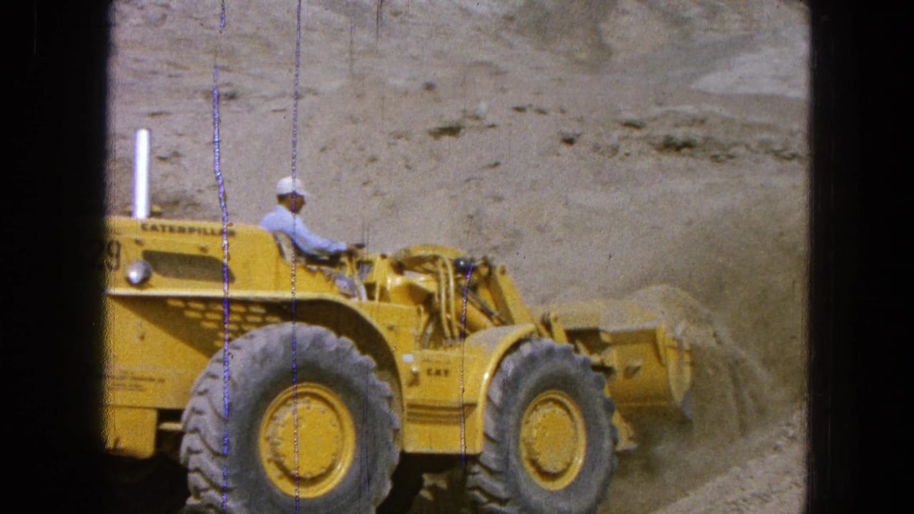 A yellow Caterpillar front-end loader is seen in profile at a dusty worksite in the 1965 Pueblo Mexico clip.