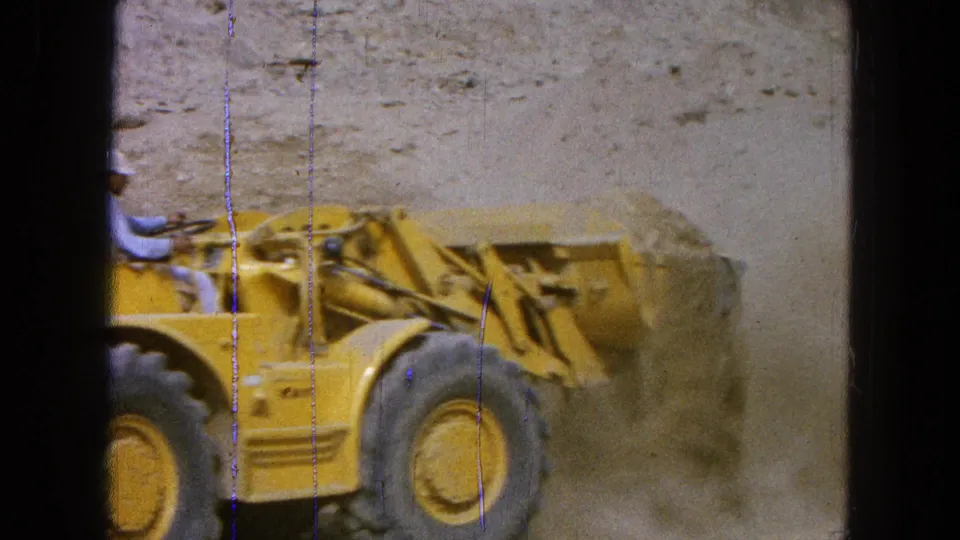 A tighter view shows the yellow loader's bucket working into a sand pile, with the operator partly cropped at the left edge.