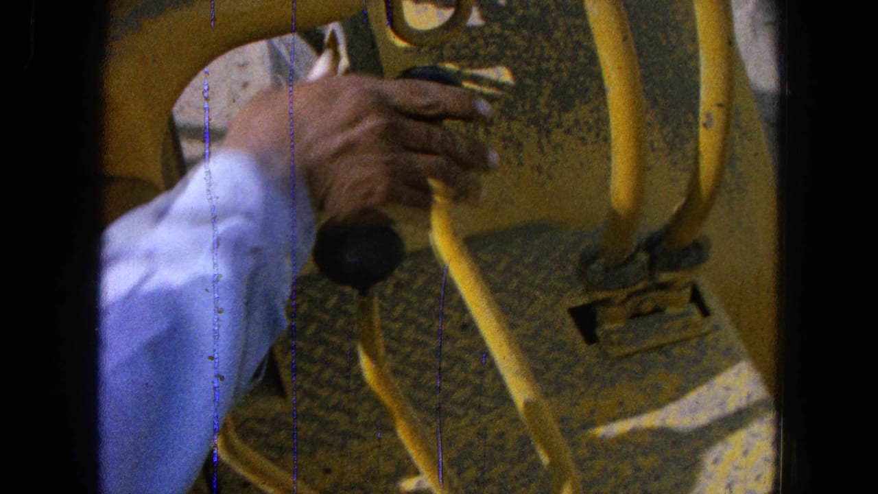 Hand in a light blue sleeve reaching toward yellow tractor controls and a black knob.