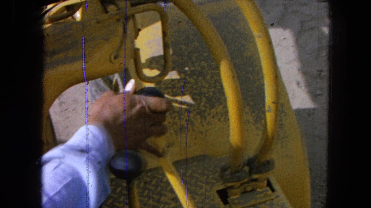 Close 8mm view of a hand gripping a black tractor control knob near yellow levers in Pueblo, Mexico, 1965.