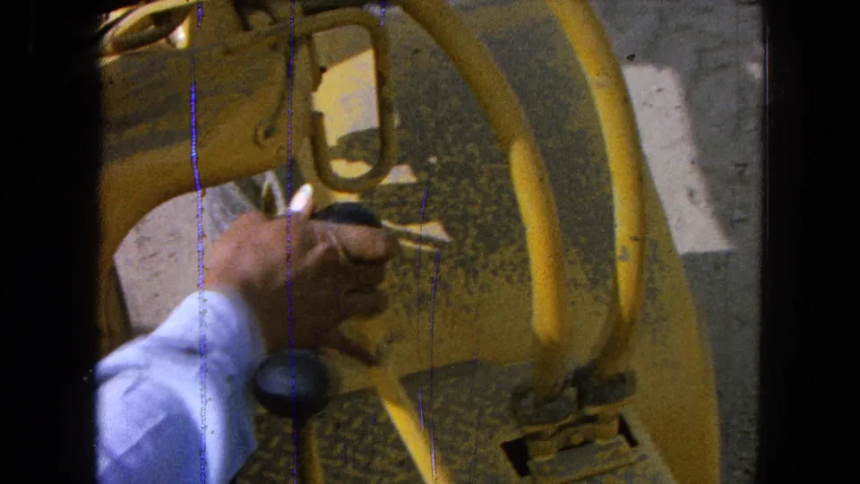 Close 8mm view of a hand gripping a black tractor control knob near yellow levers in Pueblo, Mexico, 1965.