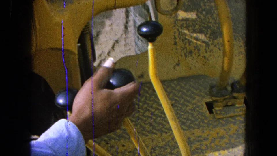 1965 close-up frame showing a hand among yellow tractor controls with two black knobs visible during mechanical instruction.