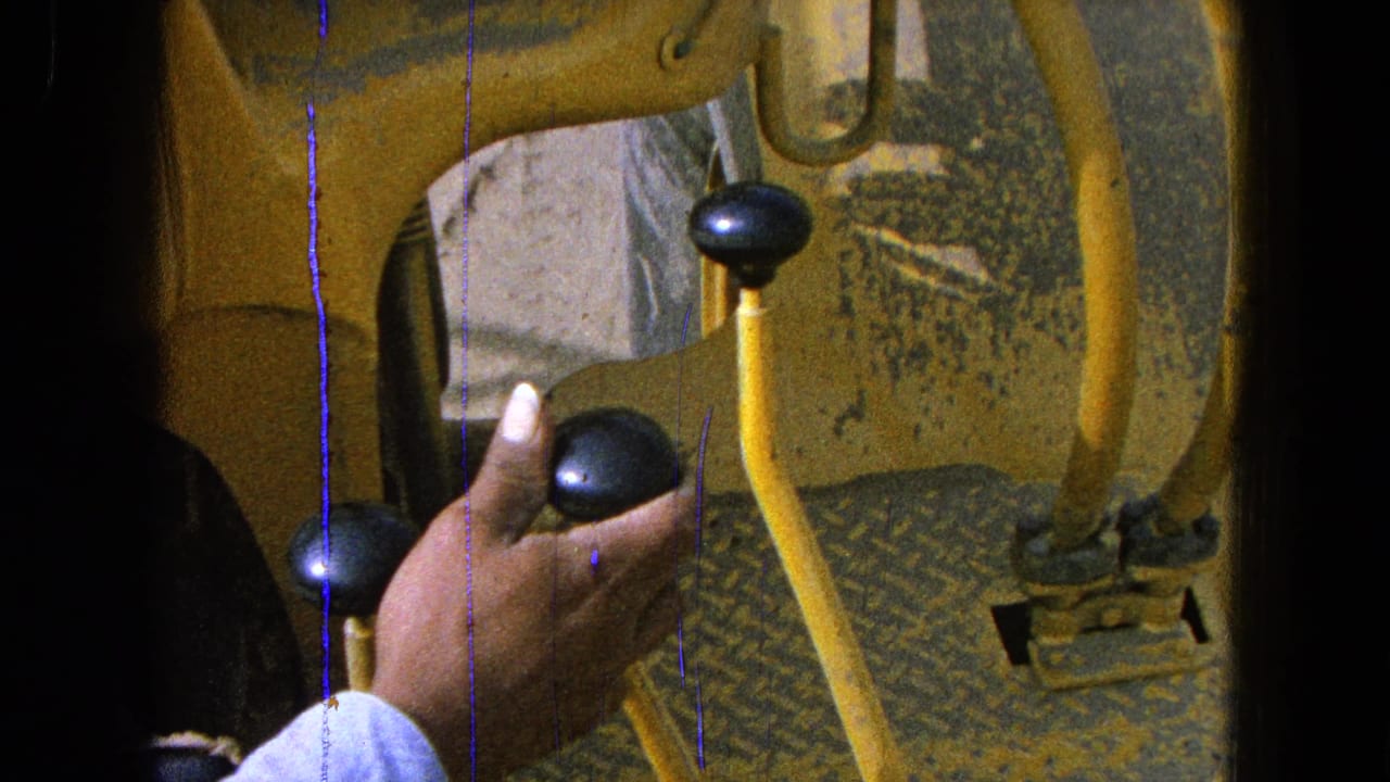 Hand in a light blue sleeve gripping a black knob on yellow machinery.
