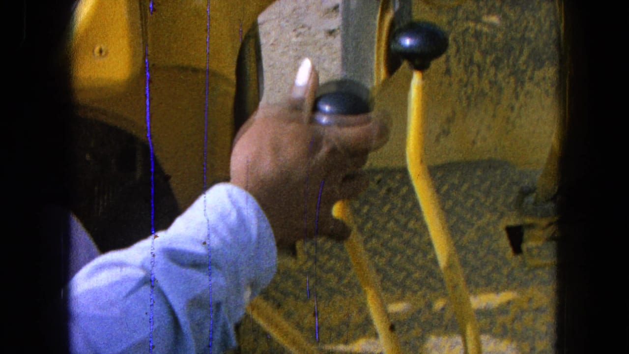 Close 8mm frame from Pueblo, Mexico in 1965 showing a hand near black control knobs on yellow machinery.
