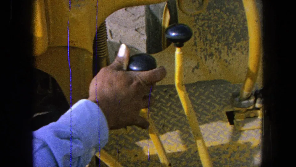 Close archival 8mm view of a hand operating yellow machinery controls, identified by metadata as Pueblo, Mexico in 1965.
