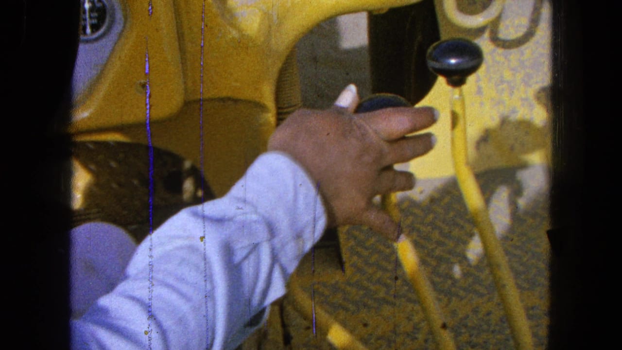 In 1965 Pueblo, Mexico footage, a hand reaches across worn yellow machinery controls with black lever knobs.
