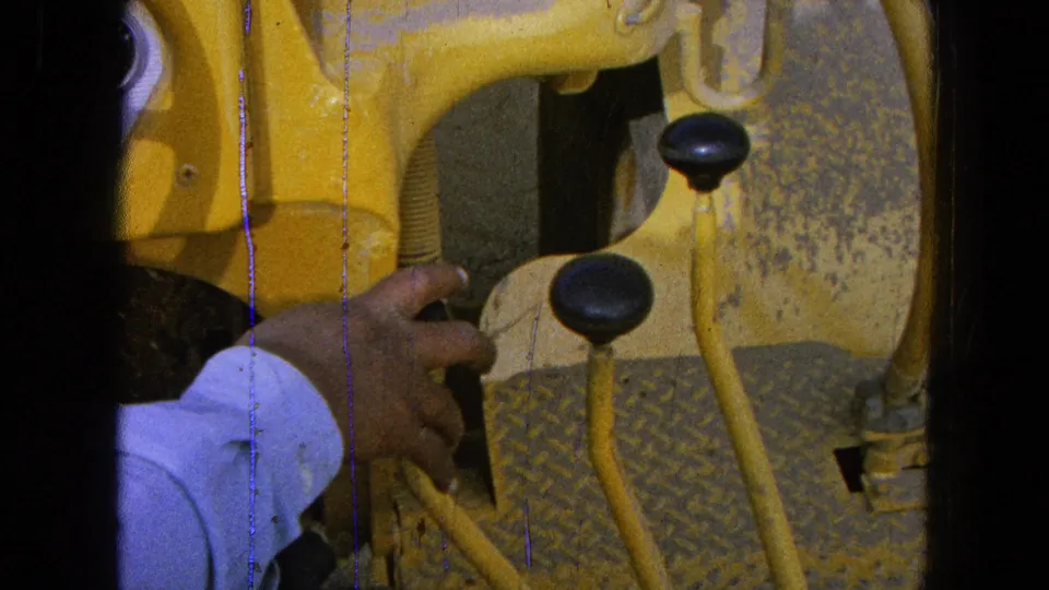 Close 8mm view of a hand working near yellow vehicle levers and black knobs in the Pueblo, Mexico clip.