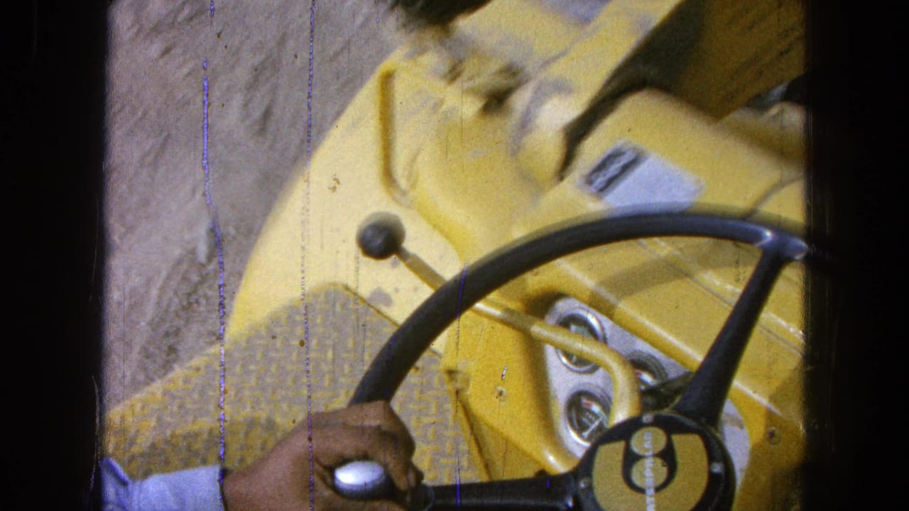 Operator's hand on a black steering wheel inside a yellow construction vehicle.