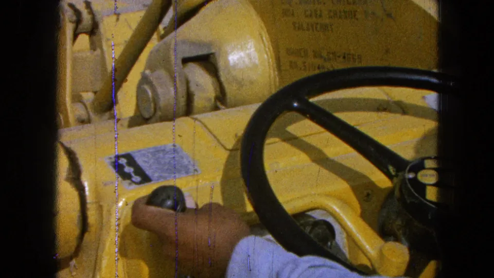 Close 8mm frame of a hand using a black control knob beside the steering wheel of yellow heavy equipment in Pueblo, Mexico.