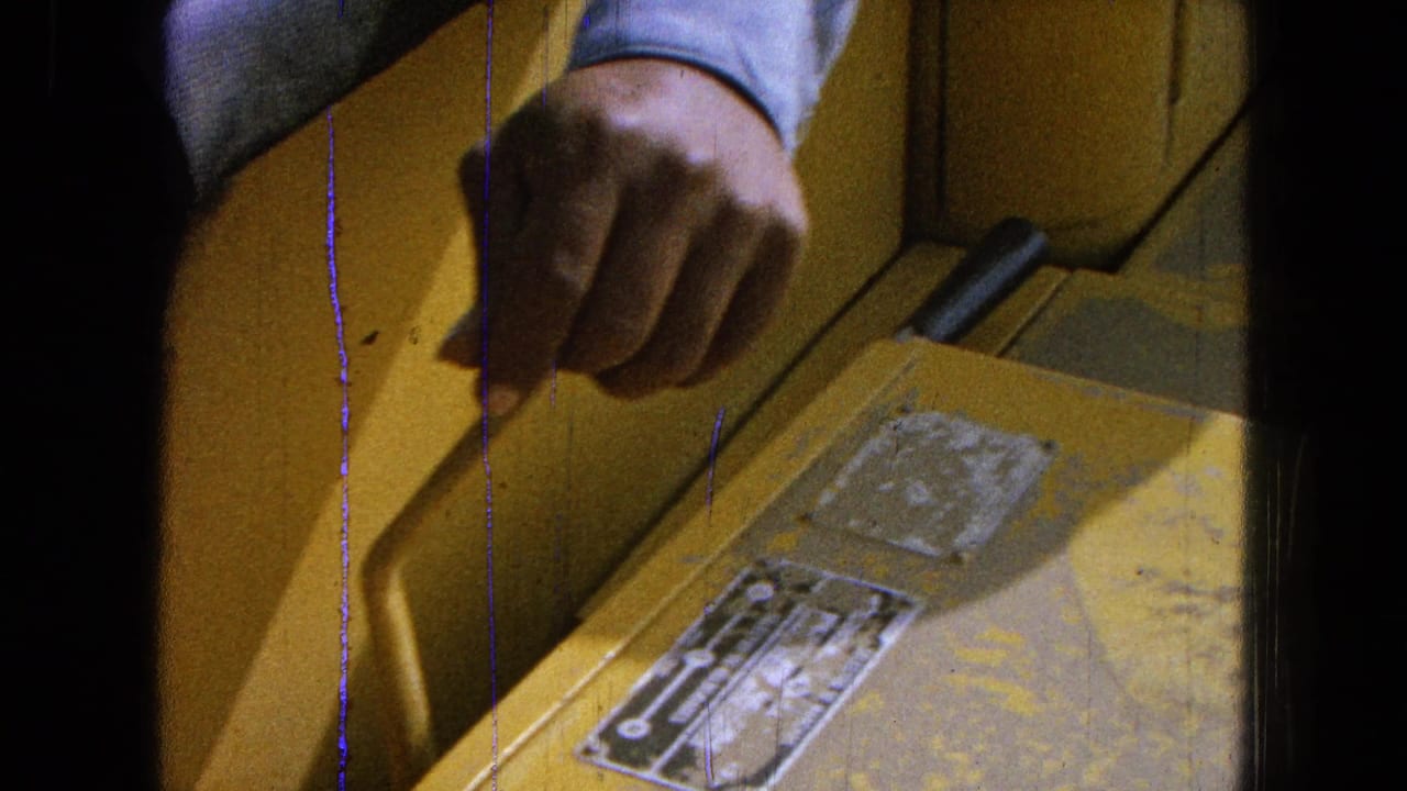 Hand in a light blue sleeve reaches over a yellow machine panel with worn labels.