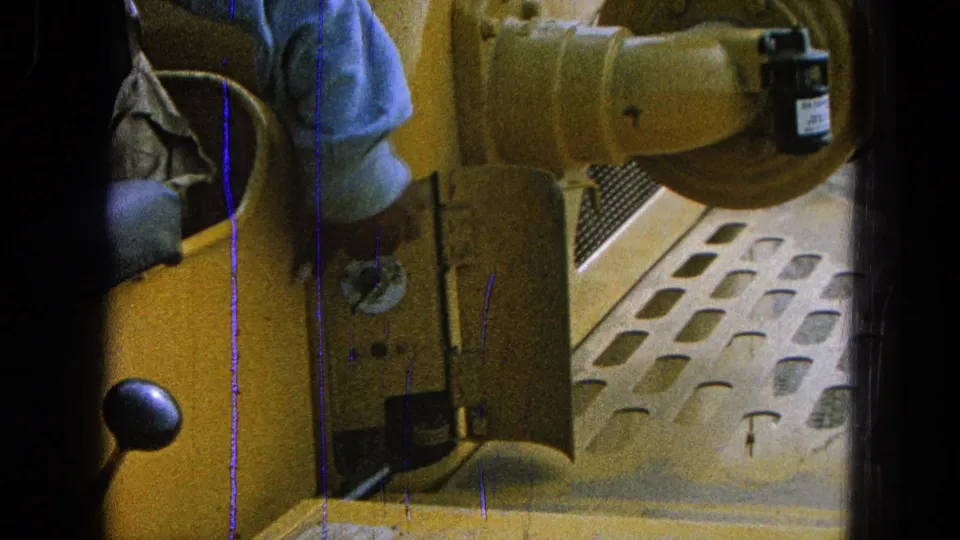 1965 Pueblo, Mexico frame showing an open small yellow door, lever knob, and metal floor inside a yellow machine or vehicle.