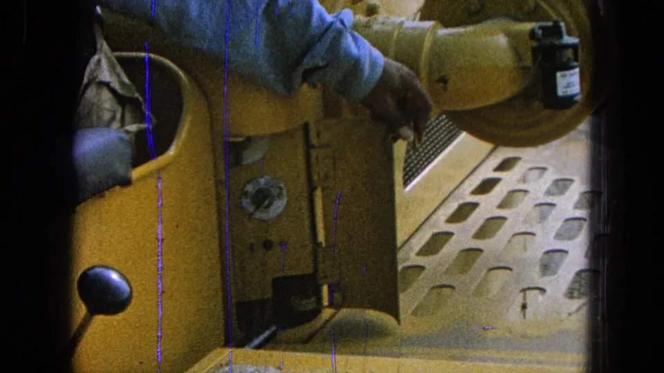 Close 8mm frame of a hand operating a control beside an open yellow panel inside machinery in Pueblo, Mexico, 1965.