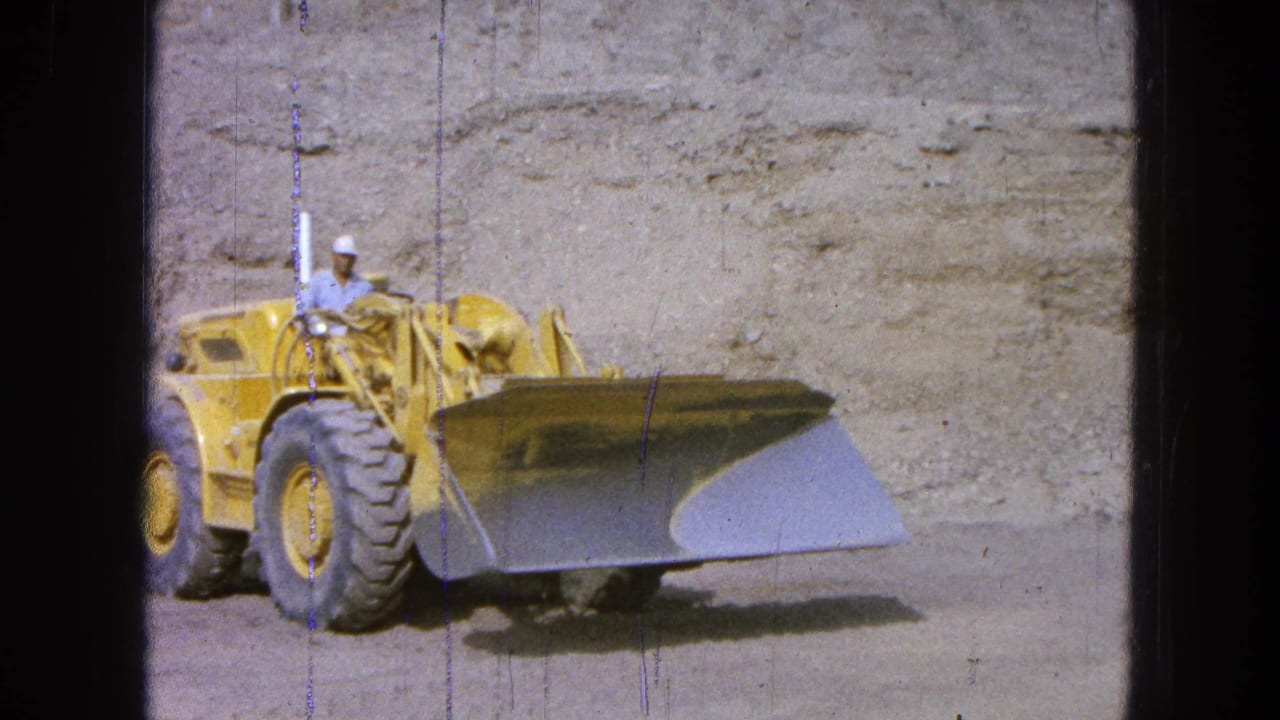 Front-end loader faces the camera with its bucket raised slightly above dusty ground.
