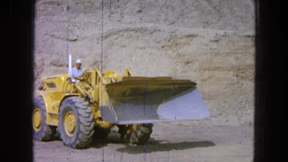 The operator guides the yellow front-end loader with its bucket lowered near the dusty surface in Pueblo, Mexico.