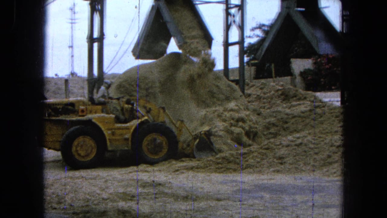 Yellow loader pushes loose material near a chute and metal supports.