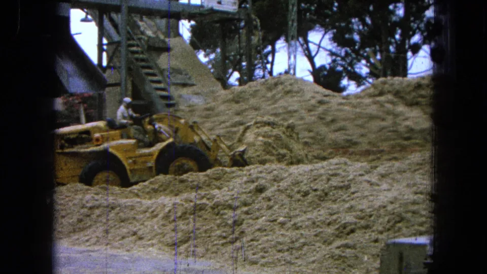 1965 Pueblo, Mexico frame with a worker operating a yellow front-end loader against a mound of pale processed material.