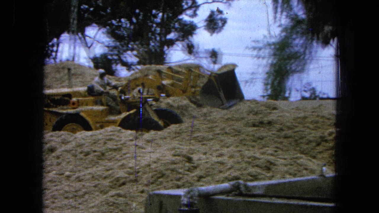 Yellow front-end loader partly hidden by sand piles at a construction site.