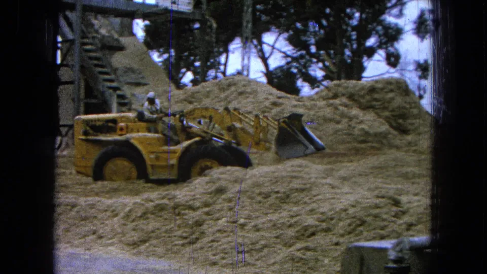 A man in a white hard hat operates a yellow front-end loader near sand piles in Pueblo, Mexico, 1965.