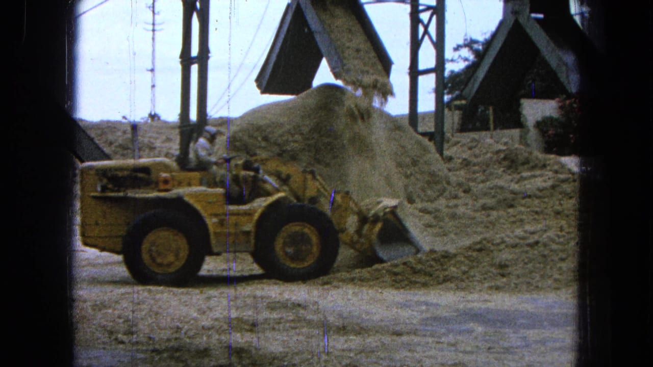 Yellow payloader beside a sawdust pile while sawdust falls from an overhead chute.