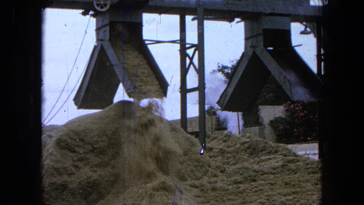 Sawdust falls onto a mound at a sawmill in this 1965 Pueblo, Mexico home-movie frame, with chute structures overhead.
