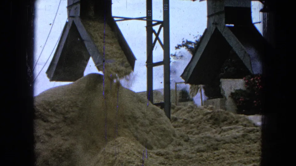 A closer 8mm view of sawdust being discharged onto a pile at the Pueblo, Mexico sawmill, with metal supports in frame.