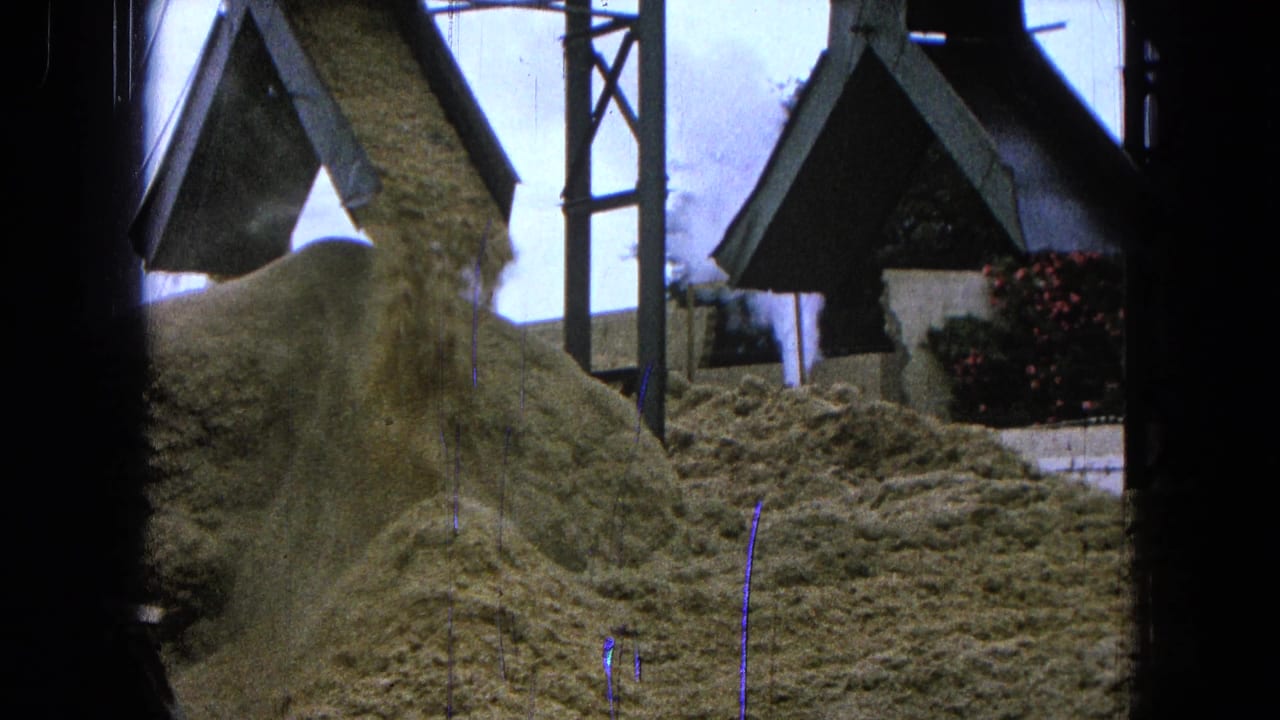 Sand or gravel falling from a conveyor near small roofed structures.