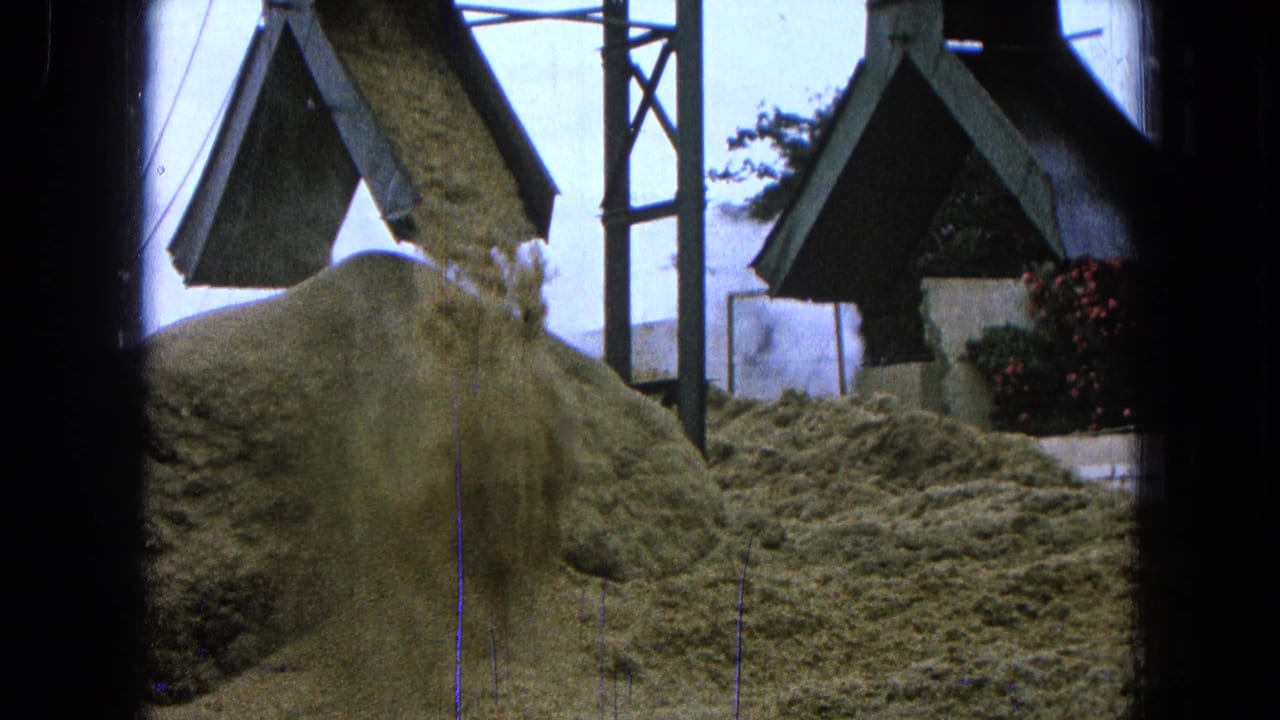 Aggregate pours from a chute onto a large pile near site structures.