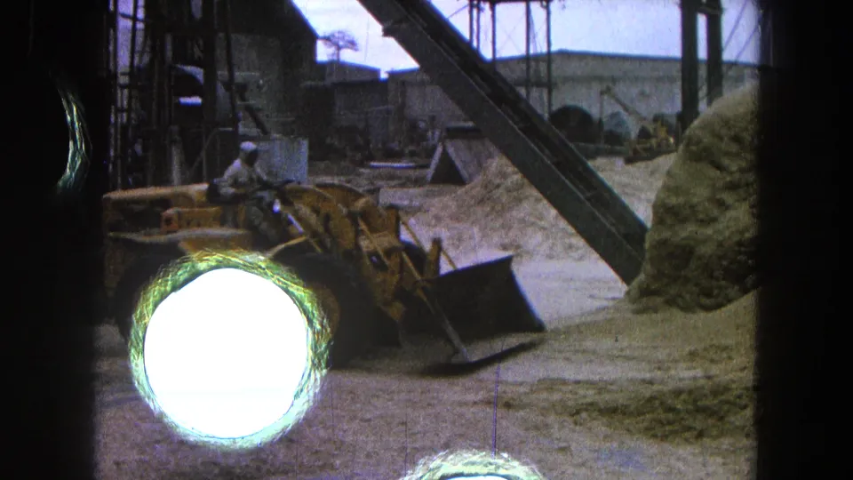 1965 Pueblo, Mexico footage shows a yellow bulldozer operating beside conveyors and aggregate piles at a construction site.