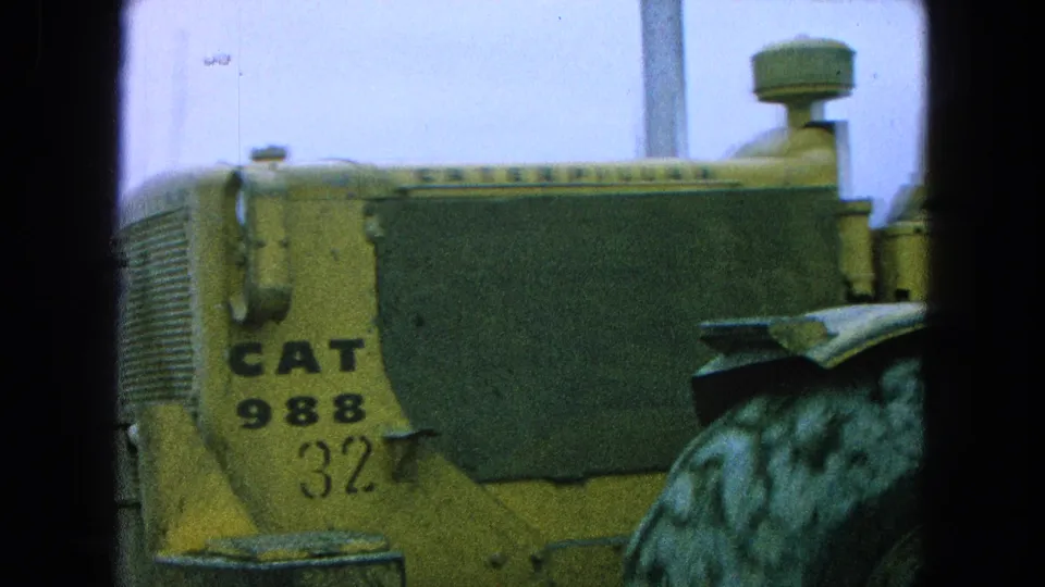 Yellow CAT 988 loader side panel with visible branding and tire detail in 1965 rural Mexico home-movie footage.