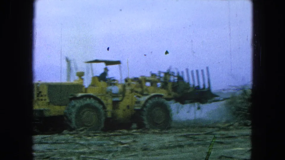 The yellow loader moves through the Pueblo, Mexico field with cut sugarcane piled in its front attachment and haze behind it.