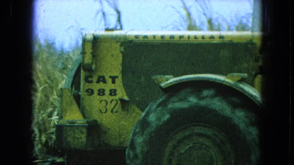 Close 8mm view of the yellow CAT 988 loader side and rear wheel, with brush or crops behind it in Pueblo Mexico.