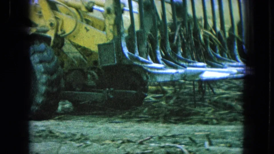 1965 Pueblo, Mexico frame showing yellow land-clearing machinery with rows of metal tines pushing through brush.