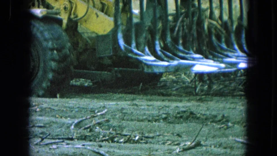 1965 Pueblo, Mexico home-movie frame of yellow heavy equipment clearing dead brush across a rural field.