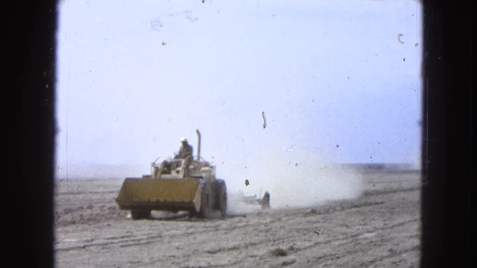 A yellow tractor works across a dry Pueblo, Mexico field in 1965, raising a dust cloud under a pale sky.