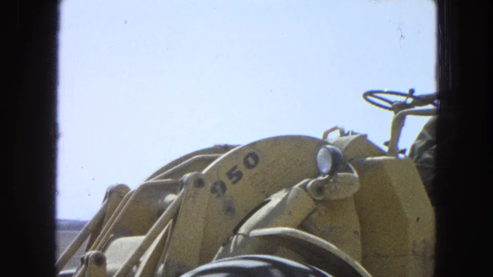 Tight 8mm frame from Pueblo, Mexico in 1965 showing the loader arm and wheel as the machine moves past the camera.