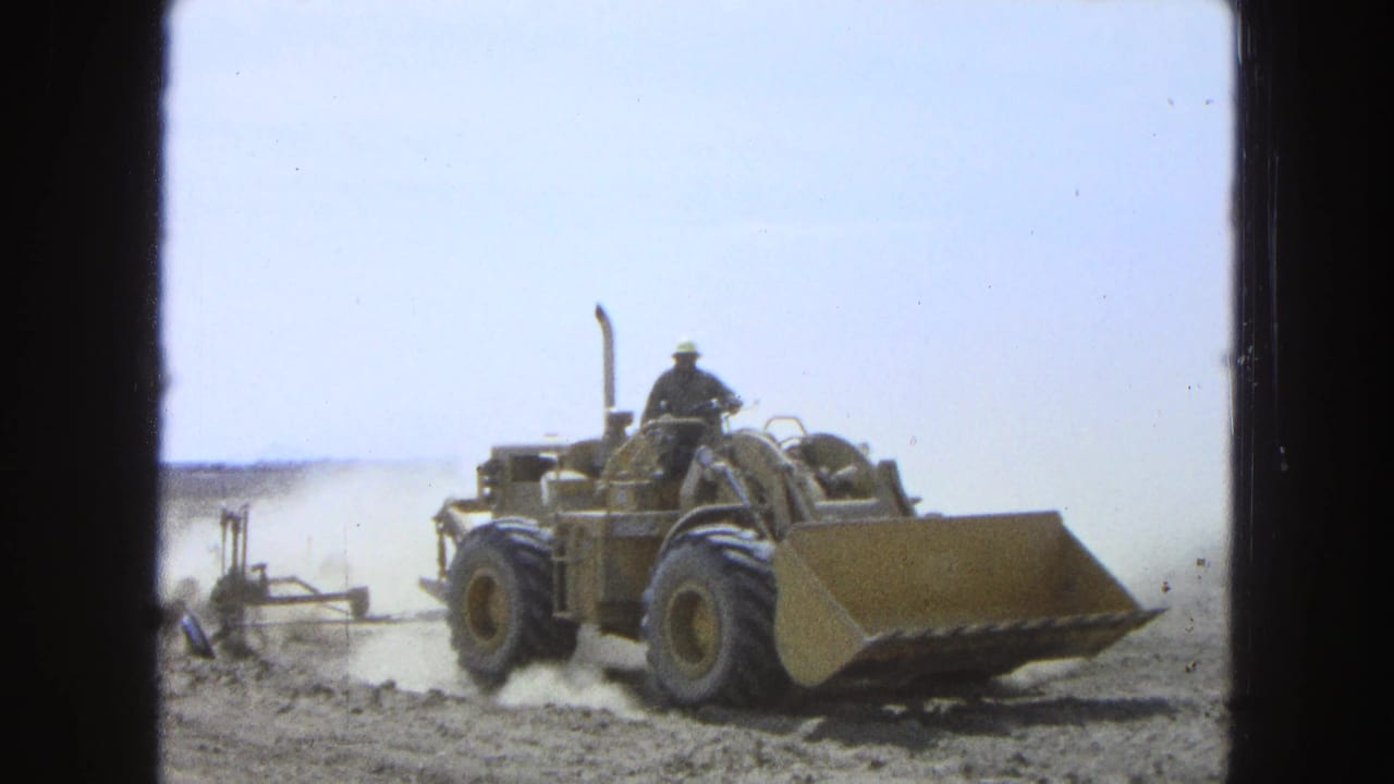 1965 Pueblo, Mexico frame with a tractor advancing through dry soil while a worker operates it from an exposed seat.
